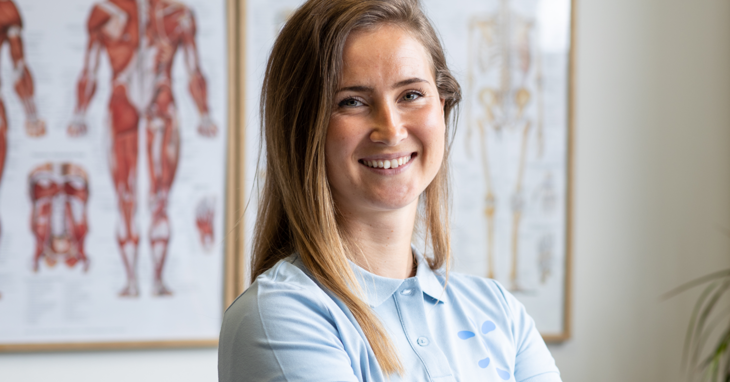 En porträttbild på fysioterapeuten Sanne som hjälper Joint Academys patienter med rätt sätt att träna. Sanne har långt brunt hår och har på sig en ljusblåa Joint Academy pikétröja. 